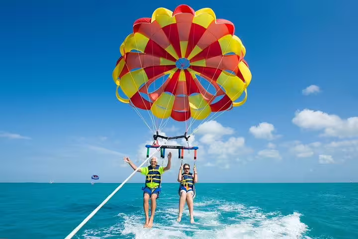 Two people enjoying parasailing in Santa Cruz de Tenerife against a bright blue sky with a colorful parachute.