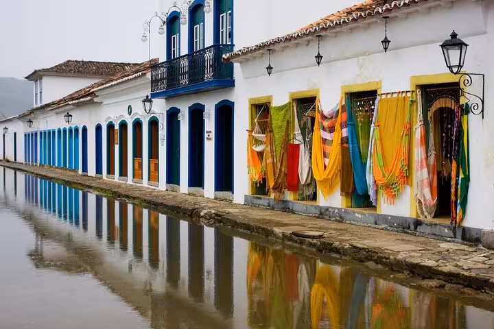 Colorful hammocks adorn colonial buildings in historic Paraty, Brazil, reflecting in a serene rain-soaked street.