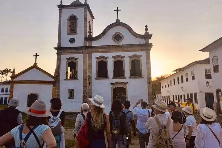 Tourists gathered at the historic Church of Our Lady of the Rosary in Paraty during sunset on a guided tour.
