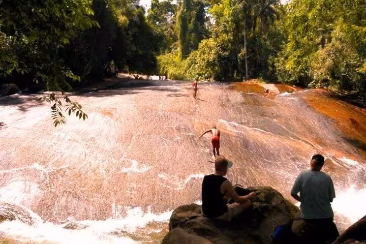 Tourists enjoying a natural waterslide at a lush forest stream in Paraty, ideal for adventurous jeep tours.