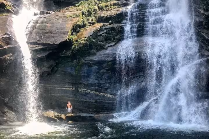 Adventurer stands beside the majestic Melancia Waterfall, showcasing its powerful cascades in Paraty's natural setting.