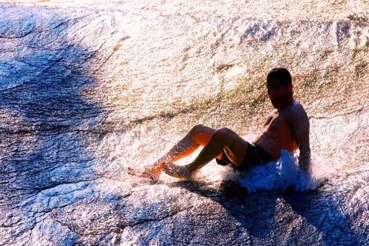 A person slides down a natural rock waterslide in Paraty, highlighted by sunlight on the private jeep tour.