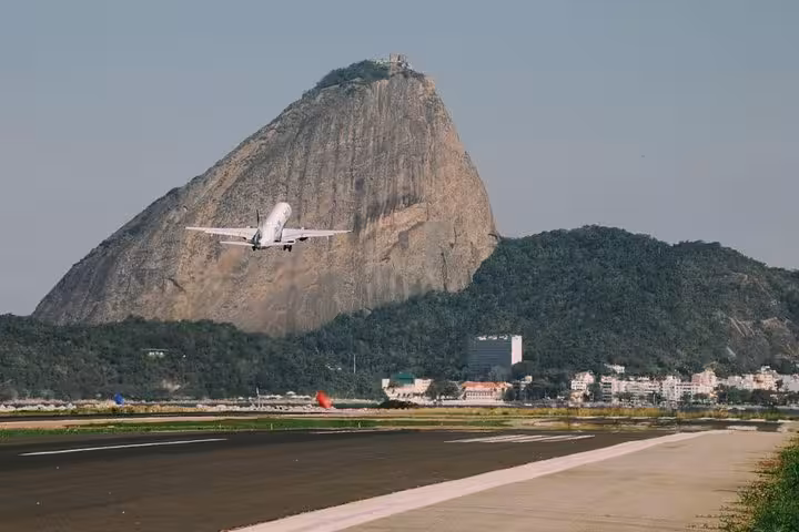 Airplane taking off at Rio airport with Sugarloaf Mountain in background, part of shared transfer experience.
