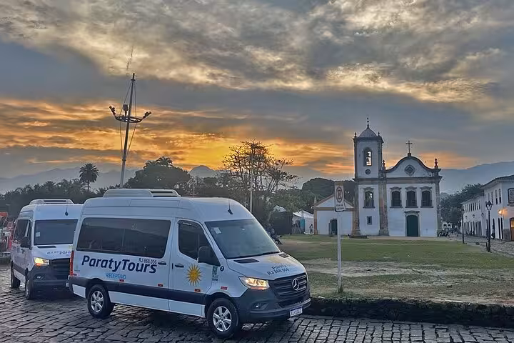 Paraty Tours vans parked near a historic church at sunrise, ready for shared transfer to Rio de Janeiro hotels.