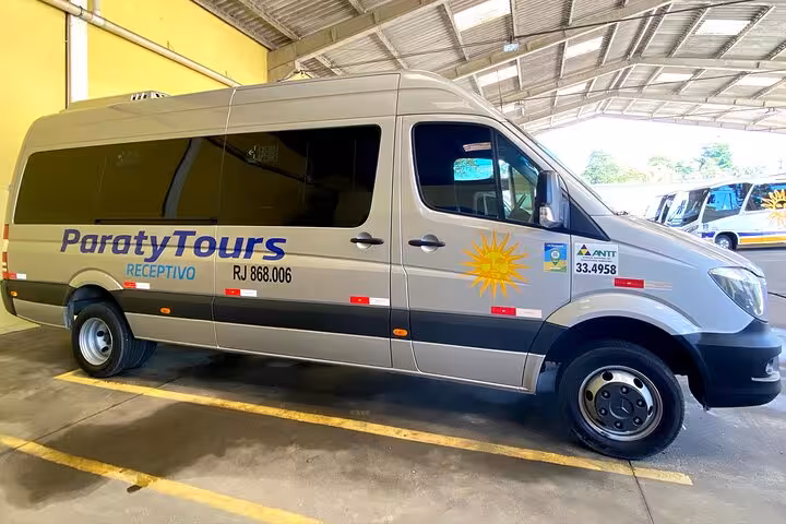 Paraty Tours shuttle bus parked in a covered area, ready for shared transfers from Angra dos Reis to Paraty.