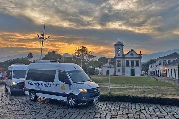 Paraty Tours shuttles parked near a historic church at sunset, highlighting scenic transfers to Ilha Grande.