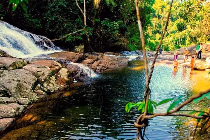 People enjoy the tranquil waters near a Paraty waterfall, surrounded by vibrant greenery and rocky landscape.