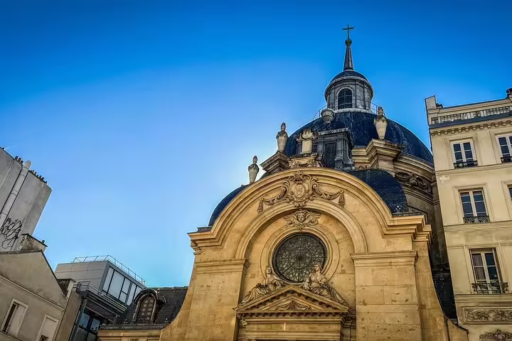 Baroque church dome with ornate facade and cross in Paris city center against blue sky