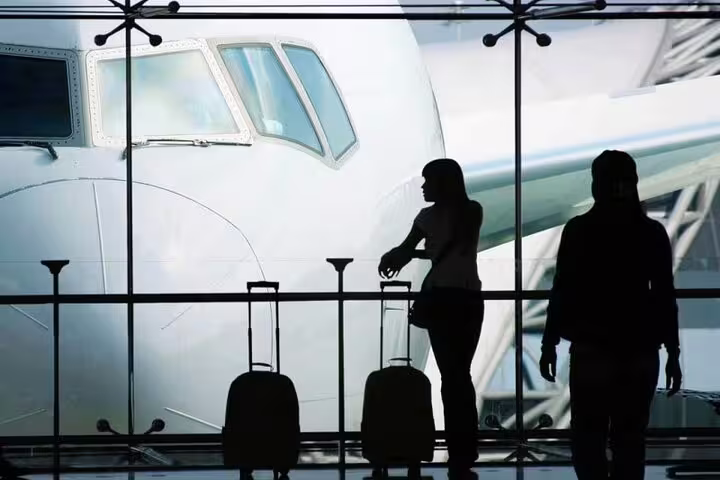 Travelers with luggage at airport terminal window, booking private Paris to Charles de Gaulle Airport transfer for 1-3 people