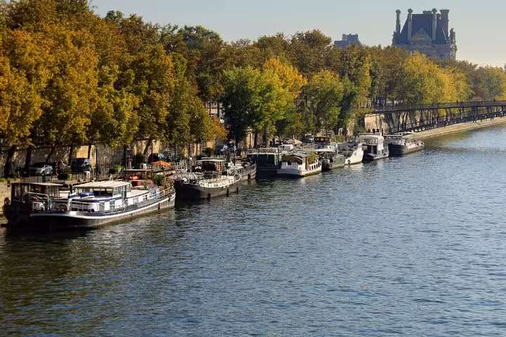 Seine riverbank with moored boats and autumn trees, scenic hop-on hop-off cruise route with Paris City Pass