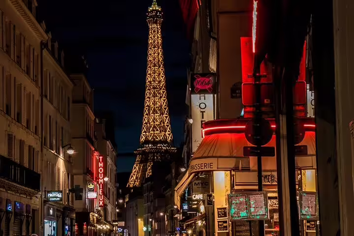 Eiffel Tower illuminated at night viewed from a bustling Paris street with glowing cafe signs