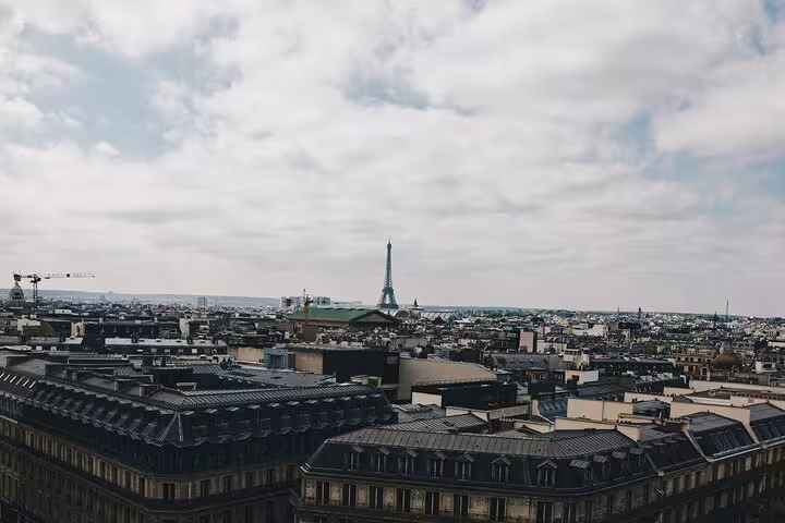 Panoramic view of Paris rooftops with Eiffel Tower visible in the distance under cloudy sky