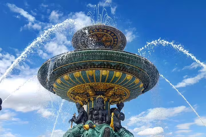 Ornate green and gold tiered fountain with bronze sculptures spraying water against blue sky in Paris