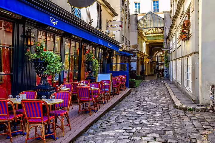 Charming Parisian café terrace with red and blue bistro chairs on a cobblestone alley in Paris