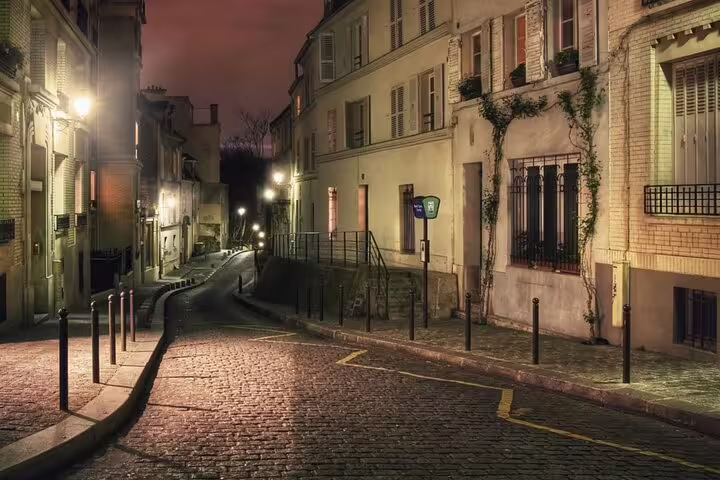 Atmospheric cobblestone street at night in Montmartre, Paris, with warm glowing streetlights and historic buildings
