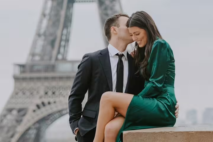 Couple sharing a kiss in front of the Eiffel Tower, woman in green dress, man in dark suit
