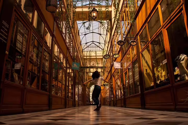 Person walking through an ornate Parisian covered arcade with glass ceiling and wooden shopfronts