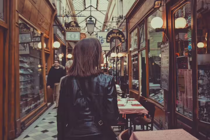 Woman in leather jacket walking through a charming Parisian covered arcade with shops