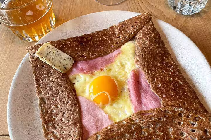 Traditional Parisian buckwheat galette with egg, ham and melted cheese on a white plate