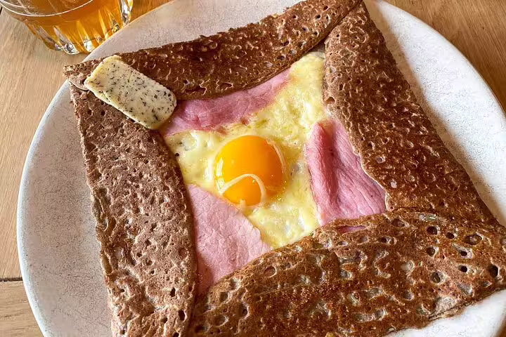 Traditional French buckwheat galette with ham, melted cheese, and sunny-side-up egg on a white plate in Paris