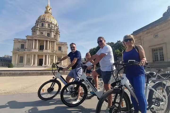 Happy riders on Paris highlights e-bike guided tour posing by Les Invalides golden dome in sunlight