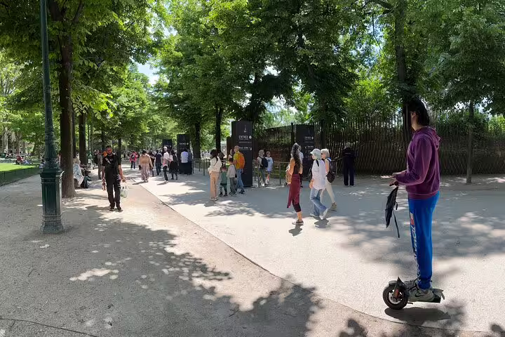 Visitors walking through a shaded Paris park pathway near Eiffel Tower entrance on a sunny day