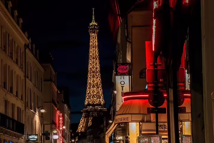 Eiffel Tower illuminated at night viewed from a Parisian street with neon-lit cafes and shops