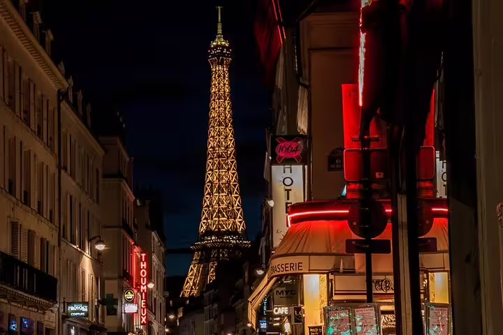 Eiffel Tower illuminated at night viewed from a Parisian street with glowing café signs
