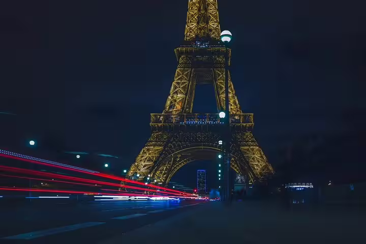 Eiffel Tower illuminated at night with colorful light trails from passing cars in Paris