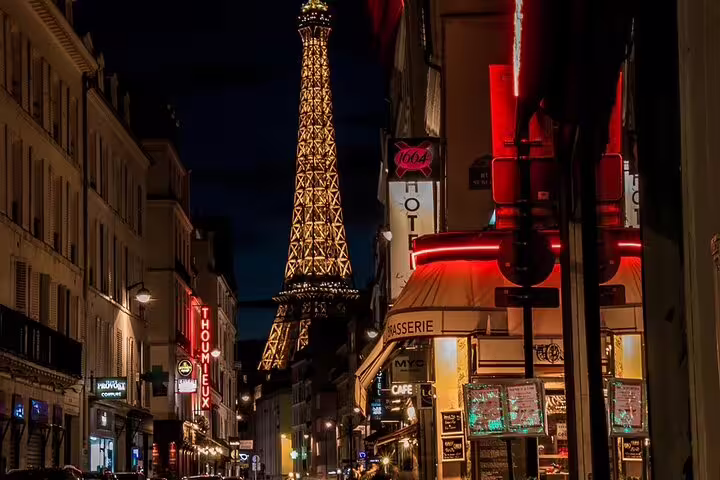 Illuminated Eiffel Tower at night viewed from a bustling Parisian street with glowing café signs