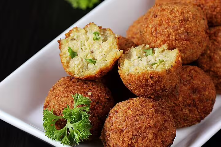 Golden crispy falafel balls on white plate, one cut open showing herbed interior, garnished with parsley