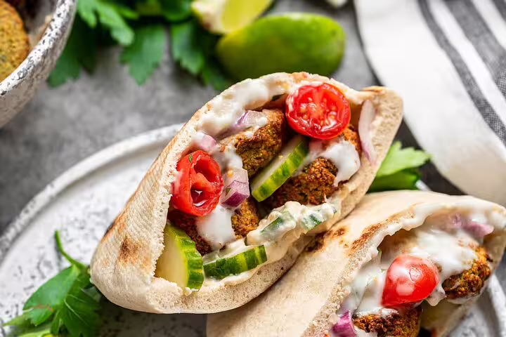 Falafel pita sandwich with cherry tomatoes, cucumber, red onion, and tahini sauce on a plate