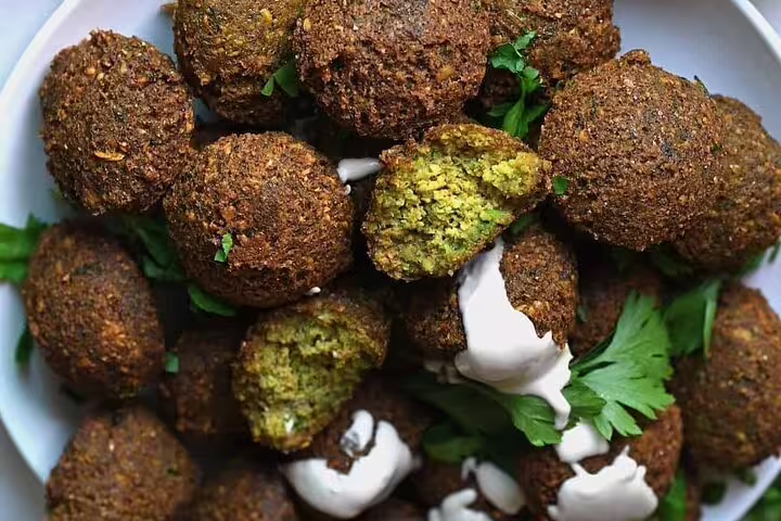 Crispy falafel balls with green herb interior served with white yogurt sauce and fresh parsley on a plate