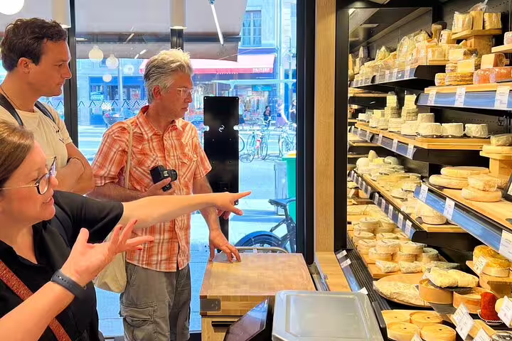 Tourists selecting cheese from a display shelf at a Paris cheese shop during a food tour