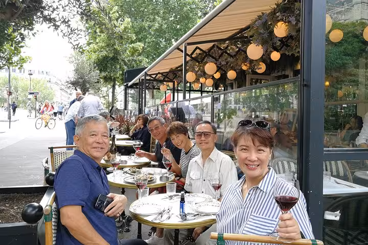 Group of tourists enjoying wine and food at a Parisian outdoor café terrace during a walking food tour