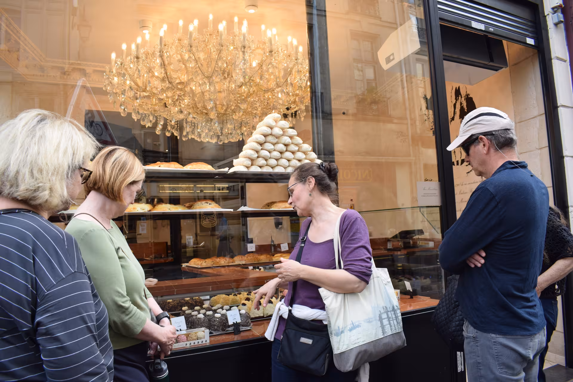 Tourists browsing pastries at a Saint-Germain-des-Prés bakery window display with chandelier