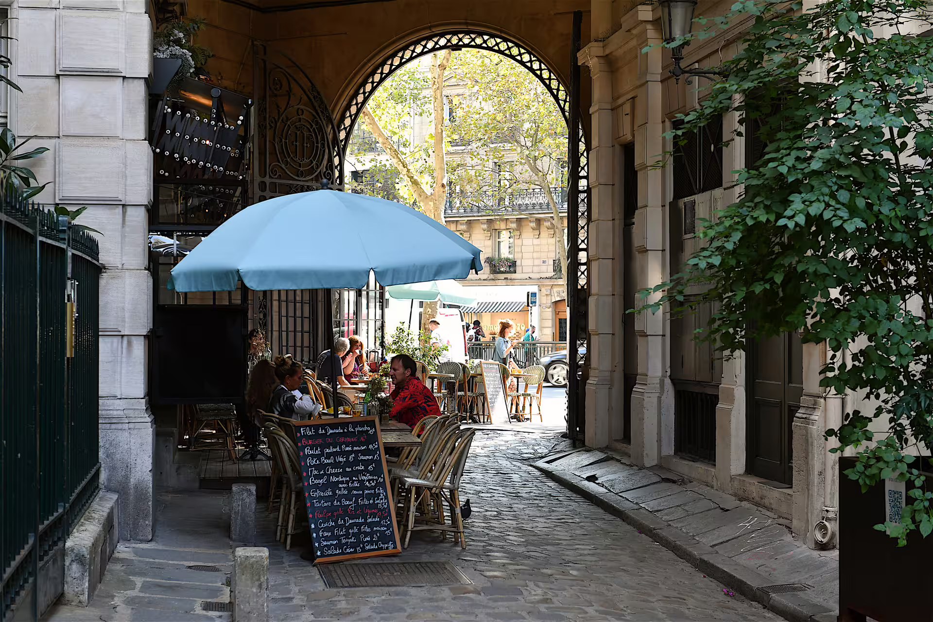 Paris café terrace under archway in a cobblestone passage, perfect stop on 1-day foodie walking tour audioguide