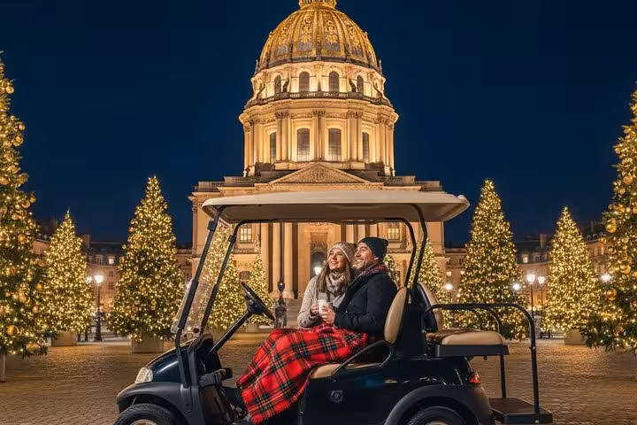 Couple on a golf cart in front of Les Invalides illuminated dome surrounded by Christmas trees at night in Paris