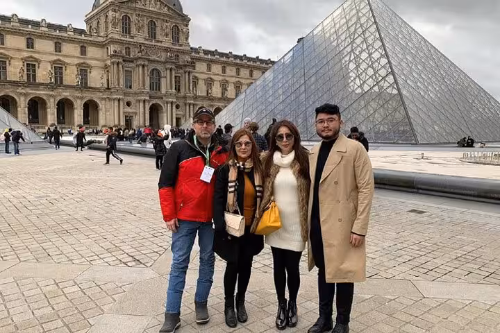 Group of four tourists posing in front of the Louvre Pyramid in Paris on a cloudy day
