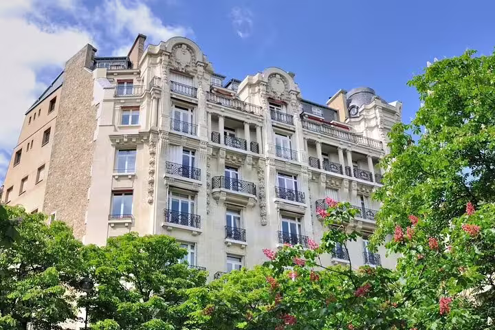 Elegant Haussmann-style Parisian apartment building framed by green trees on a clear blue sky day near the Seine