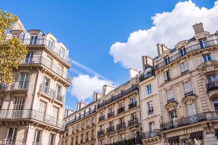 Classic Haussmann apartment buildings with wrought iron balconies under blue sky in Paris