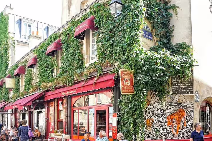 Ivy-covered Parisian café with red awnings and street art mural in Paris