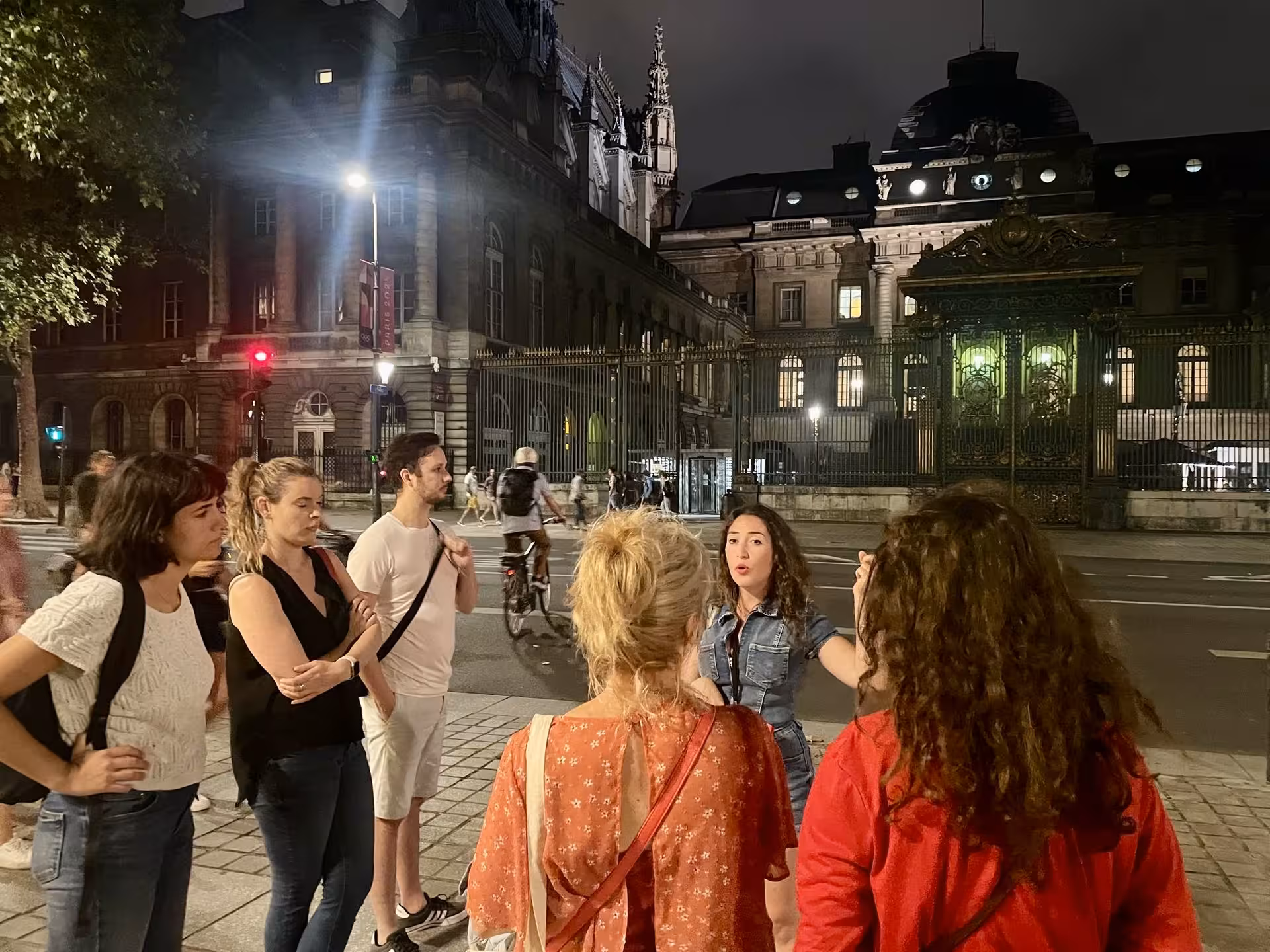 Group of tourists on a Paris night tour outside the historic Palais de Justice, illuminated under streetlights.