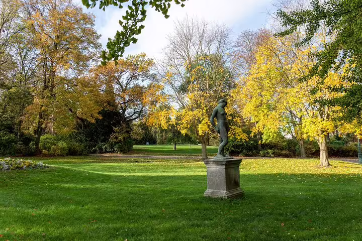 Bronze statue on pedestal in autumn Paris park with golden trees and green lawn