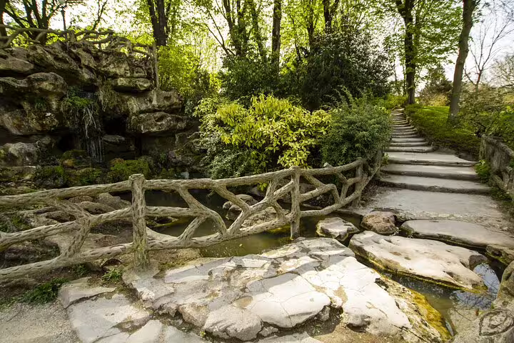 Stone bridge and steps along a lush garden path with rocky formations and water in Paris