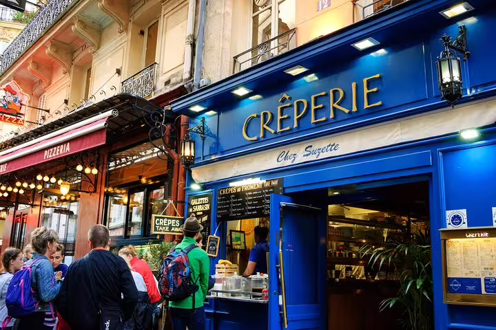 Visitors gather outside a vibrant blue crêperie in Paris' Le Marais, enjoying the authentic flavors of a French food tour.