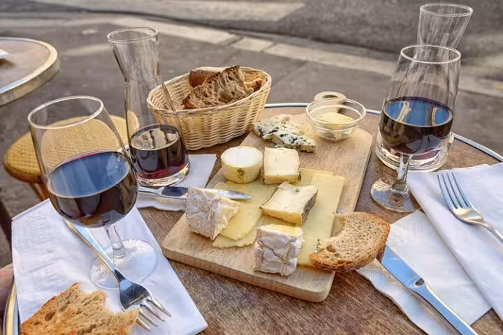 French cheese board with red wine and rustic bread on outdoor café table in Paris