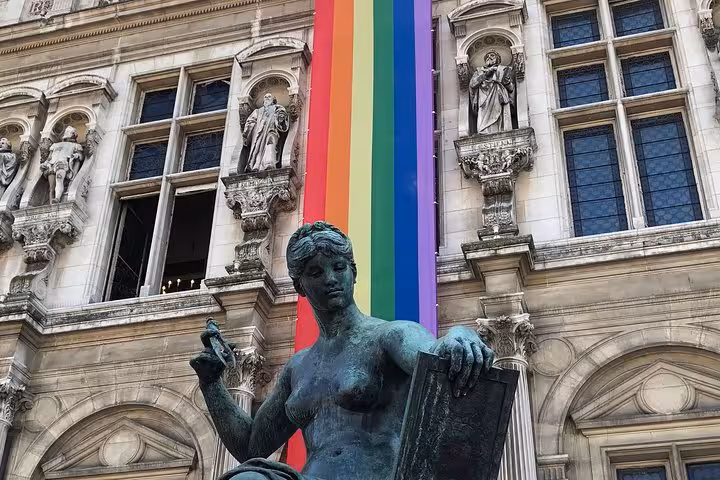 Bronze statue in front of Paris Hôtel de Ville with rainbow Pride flag draped on facade