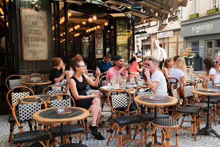 People enjoying a meal at a charming Parisian café, perfect for a break during a full-day tour of the Louvre and Sainte Chapelle.