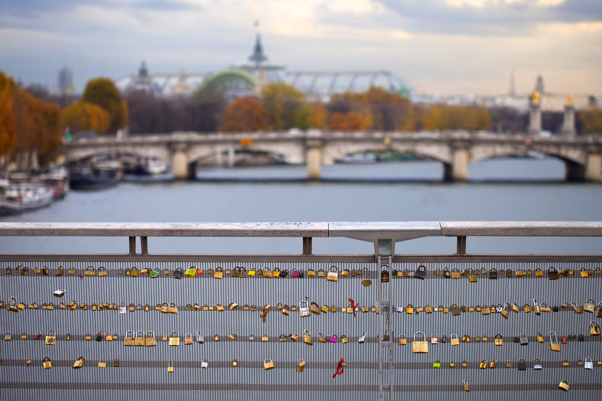 Love locks on Pont des Arts railing with Seine River bridges and Grand Palais in Paris background